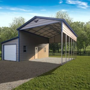 The 28x30x13/8 Vertical Roof Metal Carport with a 10' Wide Lean-To has an open-sided carport and a garage door on gravel, surrounded by lush greenery and trees beneath a bright blue sky.
