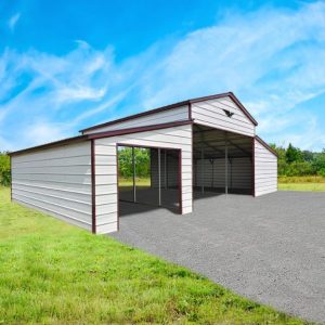 A 44x30x12/7 Vertical Roof Metal Barn With a 12' Wide Lean-To stands on gravel with open doors, set in a lush grassy field under a blue sky with wispy clouds.